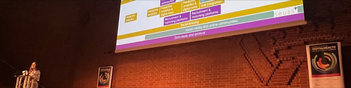Lauren Alani delivering a keynote at an industry conference, large screen behind showing the Seuss+ digital innovation framework